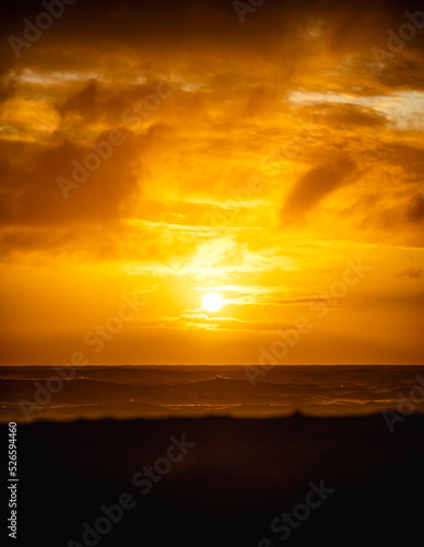 paisaje de ocaso en la playa con silueta del sol sobre el mar con olas reventando en la orilla con cielo anaranjado © Richard