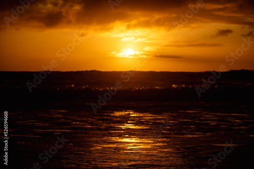 paisaje de ocaso en la playa con silueta del sol sobre el mar con olas reventando en la orilla con cielo anaranjado