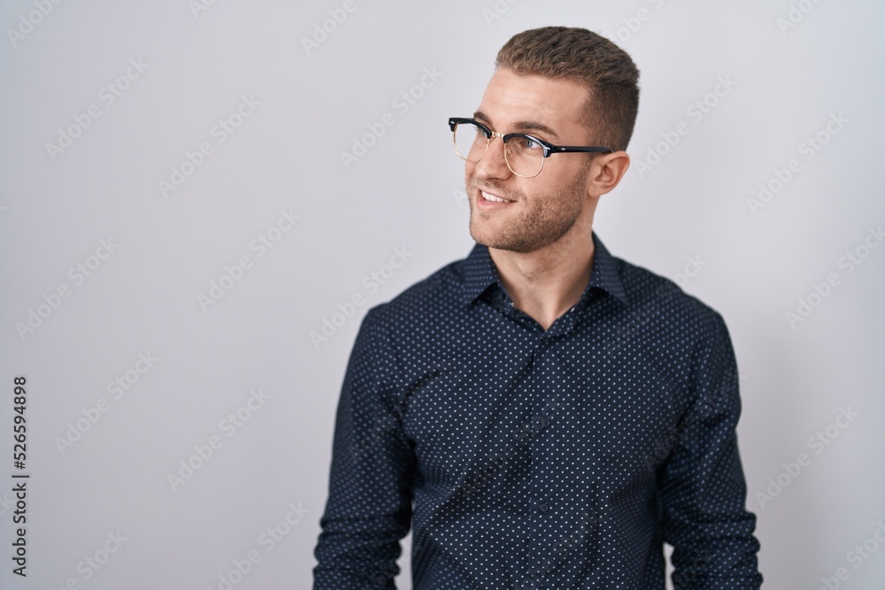 Fototapeta premium Young caucasian man standing over isolated background looking away to side with smile on face, natural expression. laughing confident.