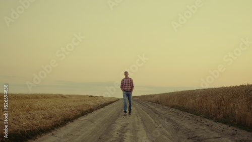Small business agronom man crossing sunset countryside with golden field alone. © stockbusters