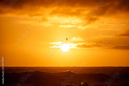 paisaje de ocaso en la playa con silueta del sol sobre el mar con olas reventando en la orilla con cielo anaranjado