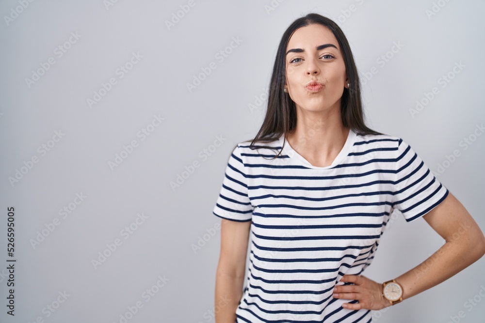Young brunette woman wearing striped t shirt looking at the camera blowing a kiss on air being lovely and sexy. love expression. Young brunette woman wearing striped t shirt looking at the camera blowing a kiss on air being lovely and sexy. love expression.