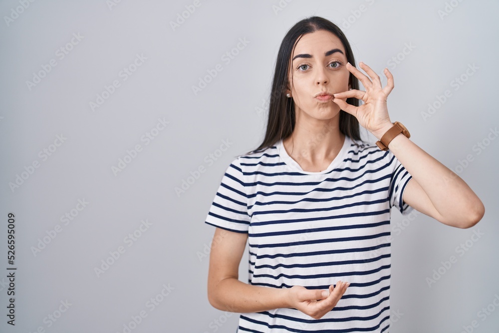 Young brunette woman wearing striped t shirt mouth and lips shut as zip with fingers. secret and silent, taboo talking Young brunette woman wearing striped t shirt mouth and lips shut as zip with fingers. secret and silent, taboo talking