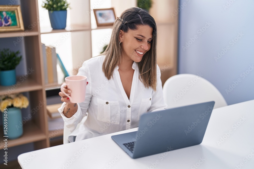 Young hispanic woman using laptop drinking coffee at home