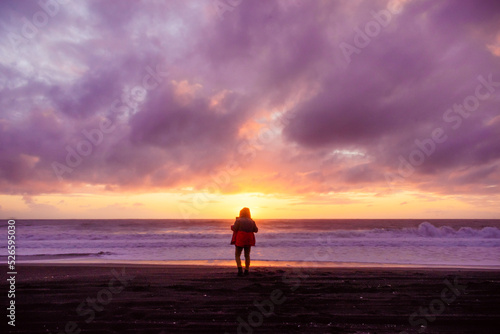 silueta de persona masculina parada en la orilla de la playa mirando al atardecer mientras el sol se oculta en el mar con nubes © Richard