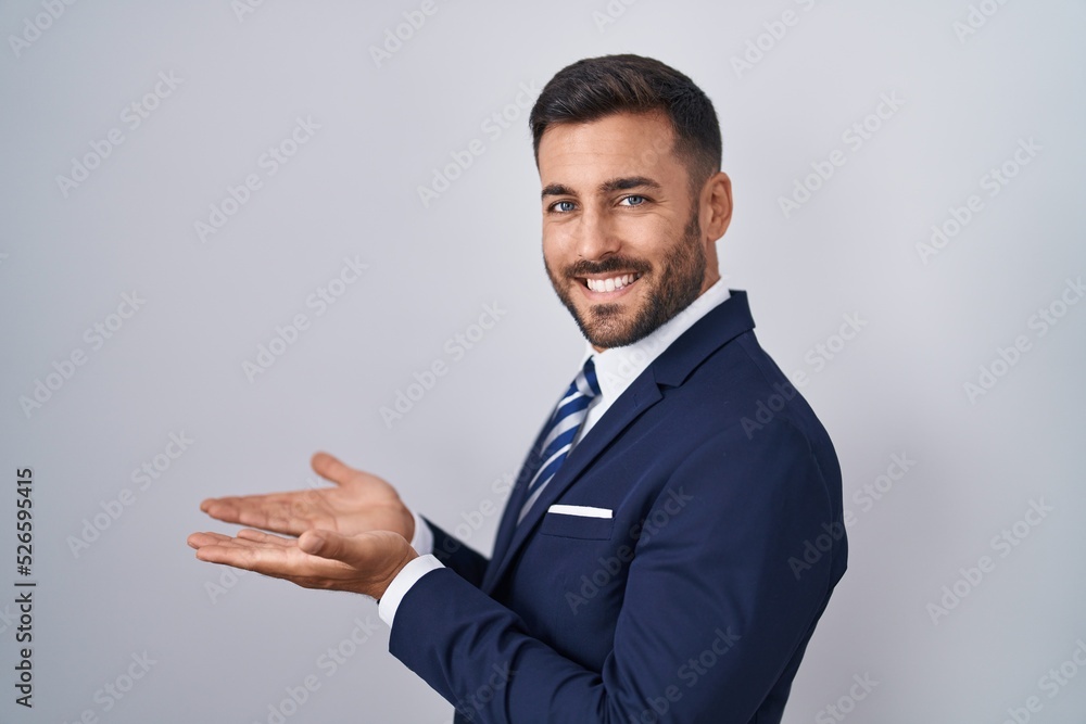 Handsome hispanic man wearing suit and tie pointing aside with hands open palms showing copy space, presenting advertisement smiling excited happy Handsome hispanic man wearing suit and tie pointing aside with hands open palms showing copy space, presenting advertisement smiling excited happy