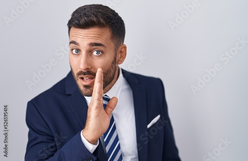 Handsome hispanic man wearing suit and tie hand on mouth telling secret rumor, whispering malicious talk conversation photo