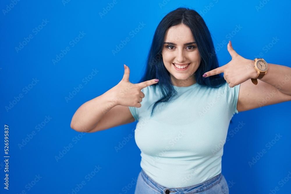 Fototapeta premium Young modern girl with blue hair standing over blue background smiling cheerful showing and pointing with fingers teeth and mouth. dental health concept.