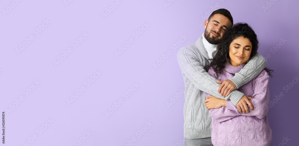 Happy young couple in autumn sweaters on lilac background with space for text Happy young couple in autumn sweaters on lilac background with space for text