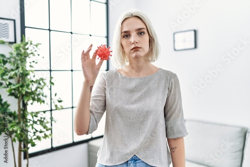 Young caucasian woman holding virus toy thinking attitude and sober expression looking self confident