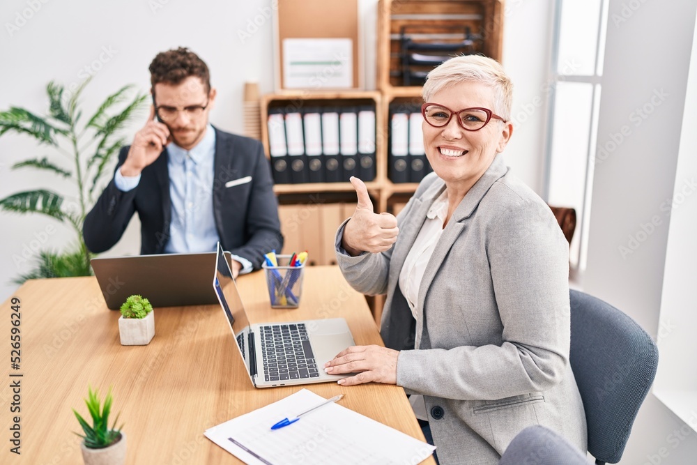 Middle age woman working at the office smiling happy and positive, thumb up doing excellent and approval sign Middle age woman working at the office smiling happy and positive, thumb up doing excellent and approval sign