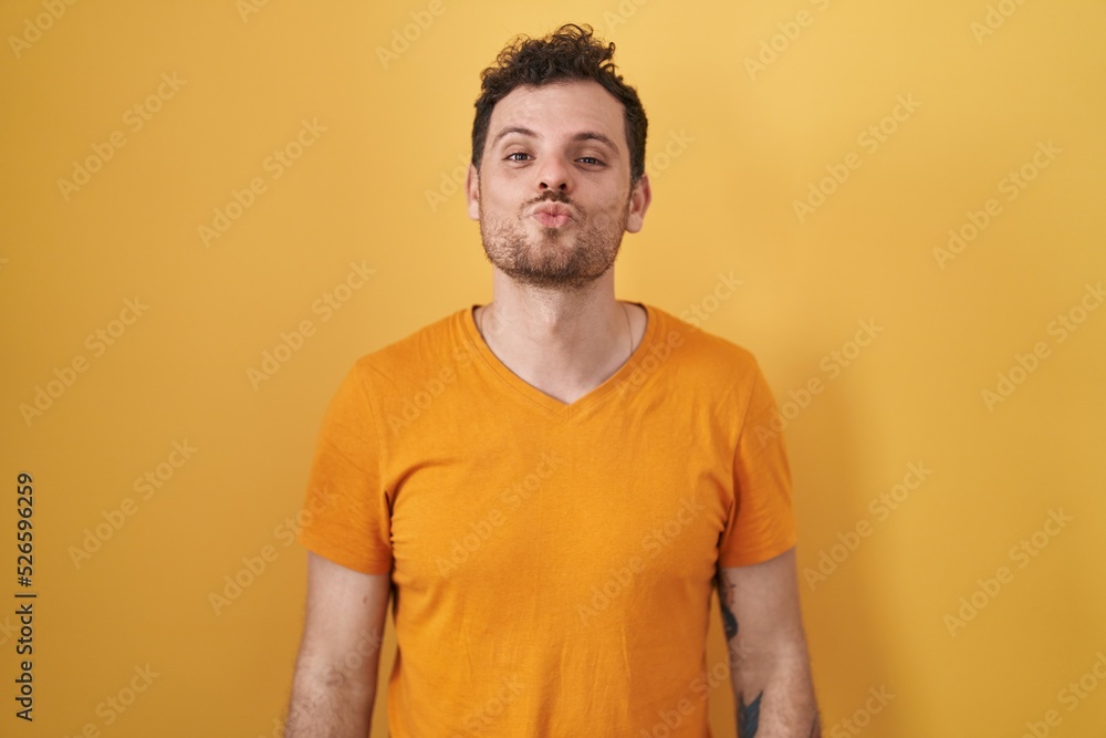 Young hispanic man standing over yellow background looking at the camera blowing a kiss on air being lovely and sexy. love expression. Young hispanic man standing over yellow background looking at the camera blowing a kiss on air being lovely and sexy. love expression.