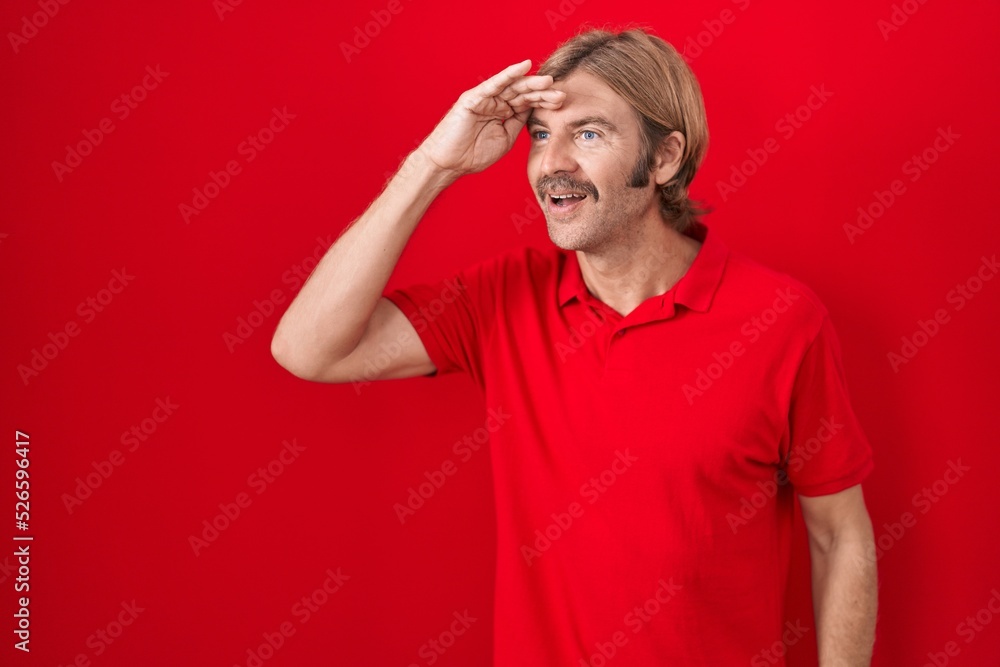 Caucasian man with mustache standing over red background very happy and smiling looking far away with hand over head. searching concept. Caucasian man with mustache standing over red background very happy and smiling looking far away with hand over head. searching concept.