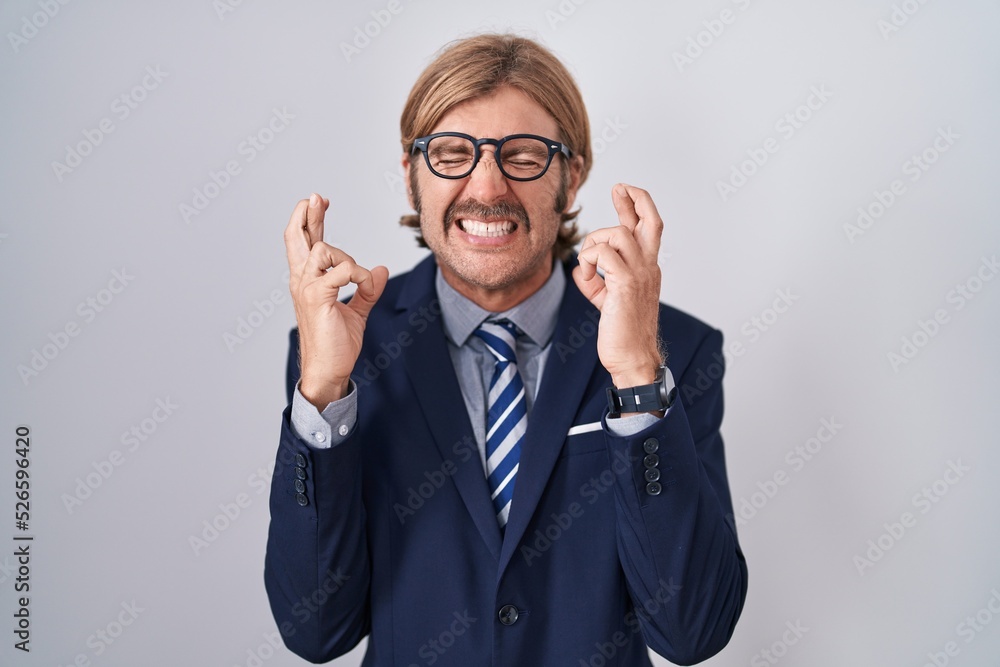 Caucasian man with mustache wearing business clothes gesturing finger crossed smiling with hope and eyes closed. luck and superstitious concept. Caucasian man with mustache wearing business clothes gesturing finger crossed smiling with hope and eyes closed. luck and superstitious concept.