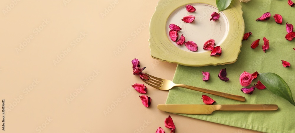 Green table setting and flower petals on beige background with space for text Green table setting and flower petals on beige background with space for text