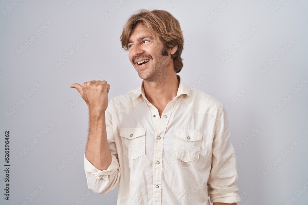Middle age man standing over isolated background smiling with happy face looking and pointing to the side with thumb up. Middle age man standing over isolated background smiling with happy face looking and pointing to the side with thumb up.