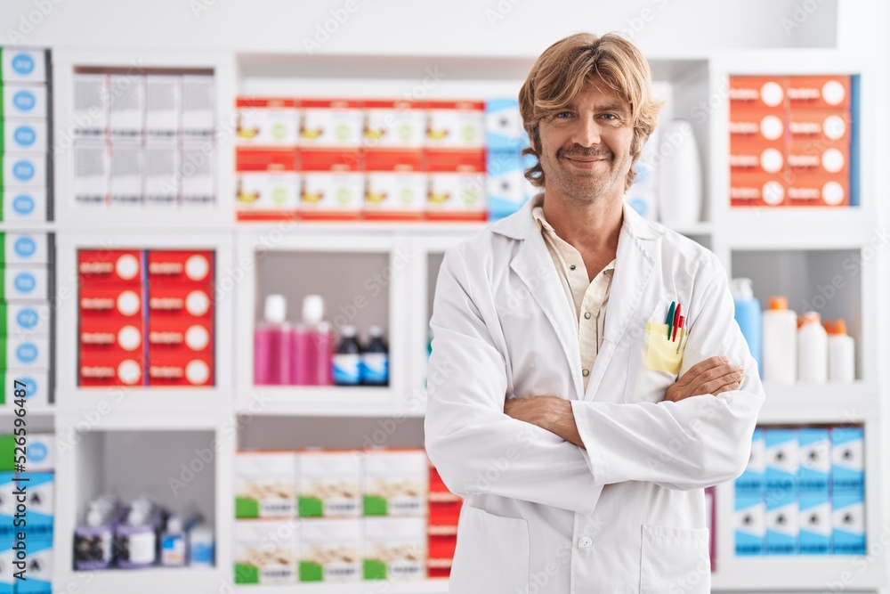 Young man pharmacist smiling confident standing with arms crossed gesture at pharmacy