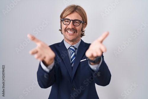 Caucasian man with mustache wearing business clothes smiling cheerful offering hands giving assistance and acceptance.