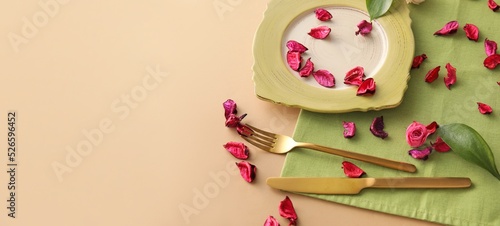 Green table setting and flower petals on beige background with space for text