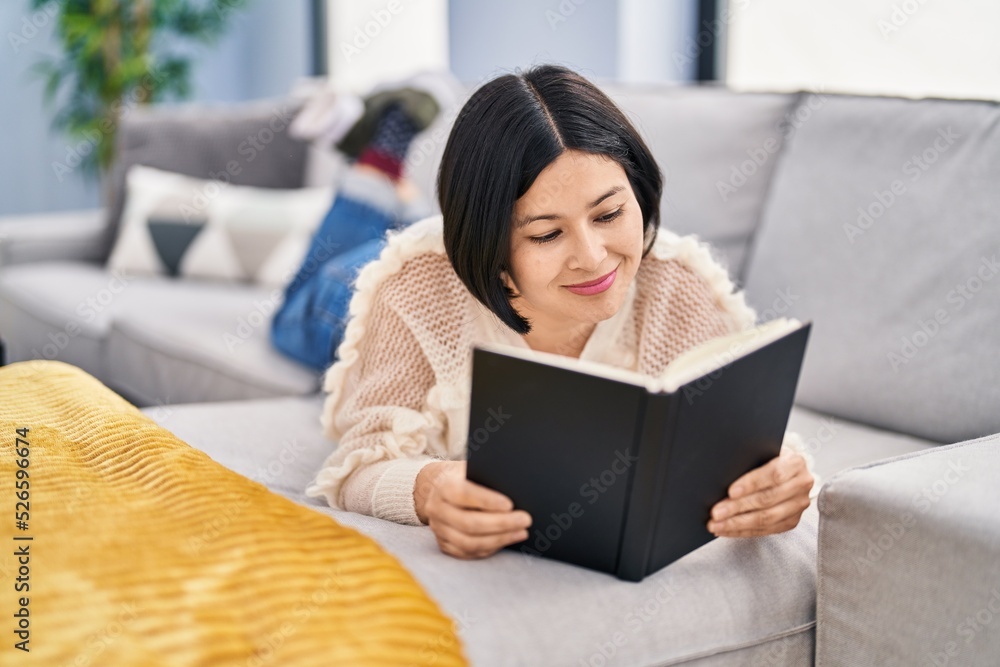 Young chinese woman reading book lying on sofa at home Young chinese woman reading book lying on sofa at home