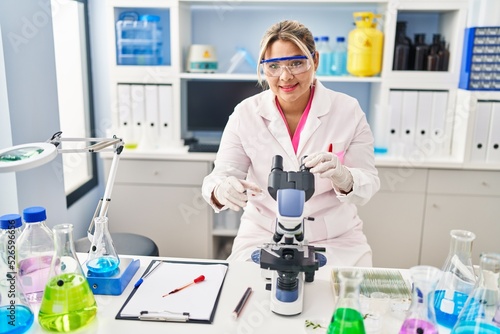 Young hispanic woman wearing scientist uniform analysing blood at laboratory