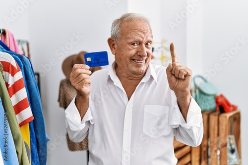 Senior man at retail shop holding credit card smiling with an idea or question pointing finger with happy face, number one © Krakenimages.com