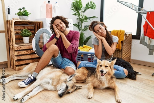 Young hispanic couple doing laundry with dogs sleeping tired dreaming and posing with hands together while smiling with closed eyes.