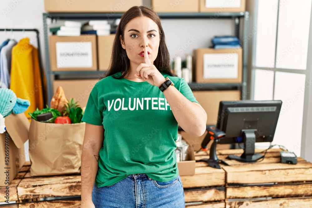 Young brunette woman wearing volunteer t shirt at donations stand asking to be quiet with finger on lips. silence and secret concept. Young brunette woman wearing volunteer t shirt at donations stand asking to be quiet with finger on lips. silence and secret concept.