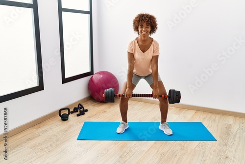 Young african american woman smiling confident training using dumbbell at sport center