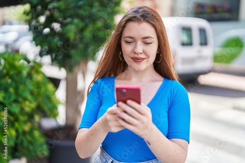 Young redhead woman smiling confident using smartphone at street