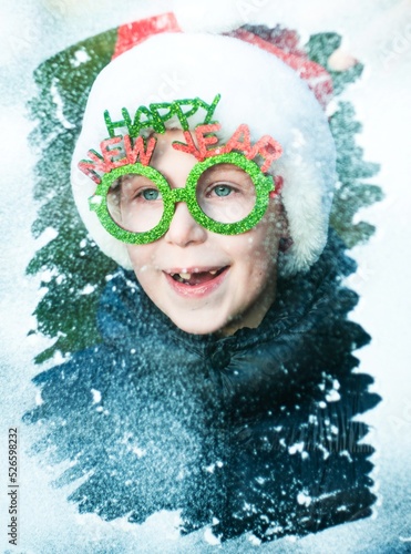 Fototapeta Naklejka Na Ścianę i Meble -  boy in santa claus costume looking throught the snowy window, happy new year concept