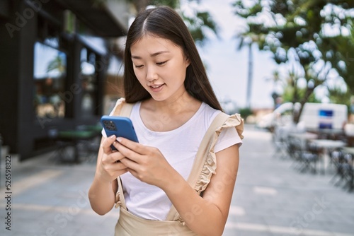 Young chinese girl smiling happy using smartphone at the city.