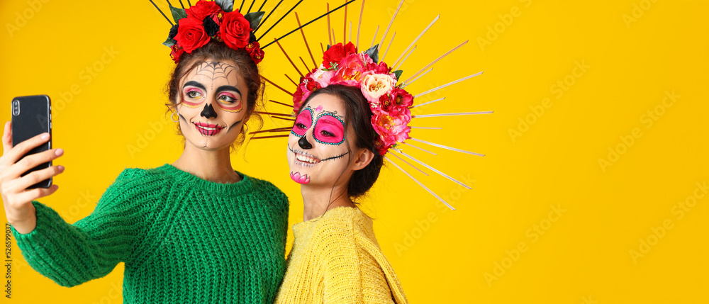 Women with painted skull on faces taking selfie against yellow background with space for text. Halloween celebration Women with painted skull on faces taking selfie against yellow background with space for text. Halloween celebration