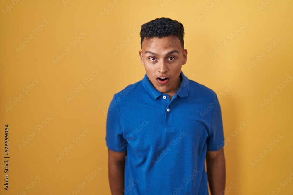Young hispanic man standing over yellow background afraid and shocked with surprise and amazed expression, fear and excited face. Young hispanic man standing over yellow background afraid and shocked with surprise and amazed expression, fear and excited face.