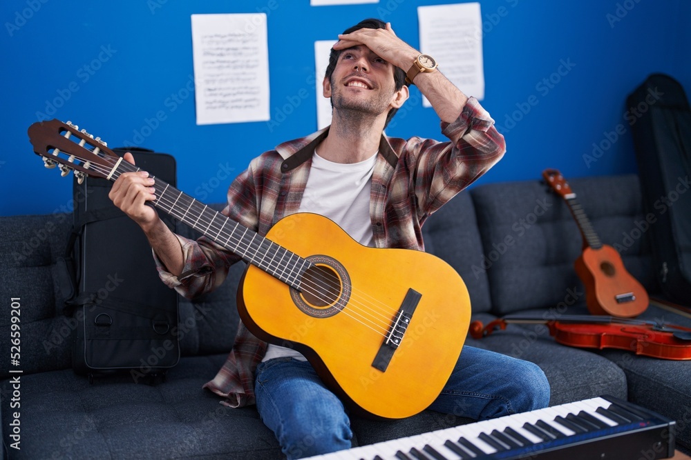 Obraz premium Young hispanic man playing classic guitar at music studio stressed and frustrated with hand on head, surprised and angry face