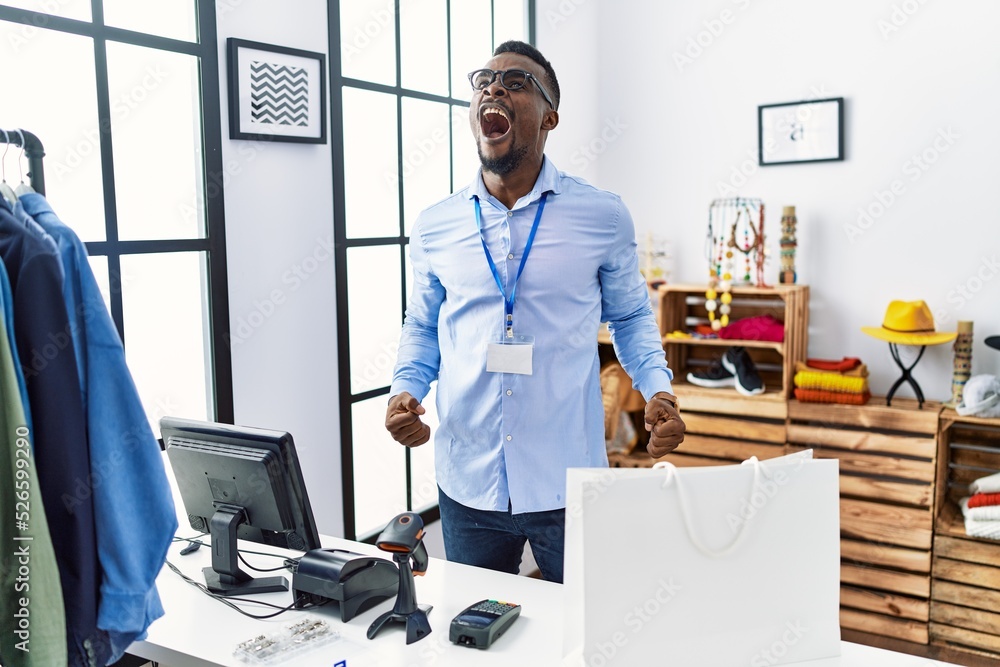 Young african man working as manager at retail boutique angry and mad screaming frustrated and furious, shouting with anger. rage and aggressive concept.