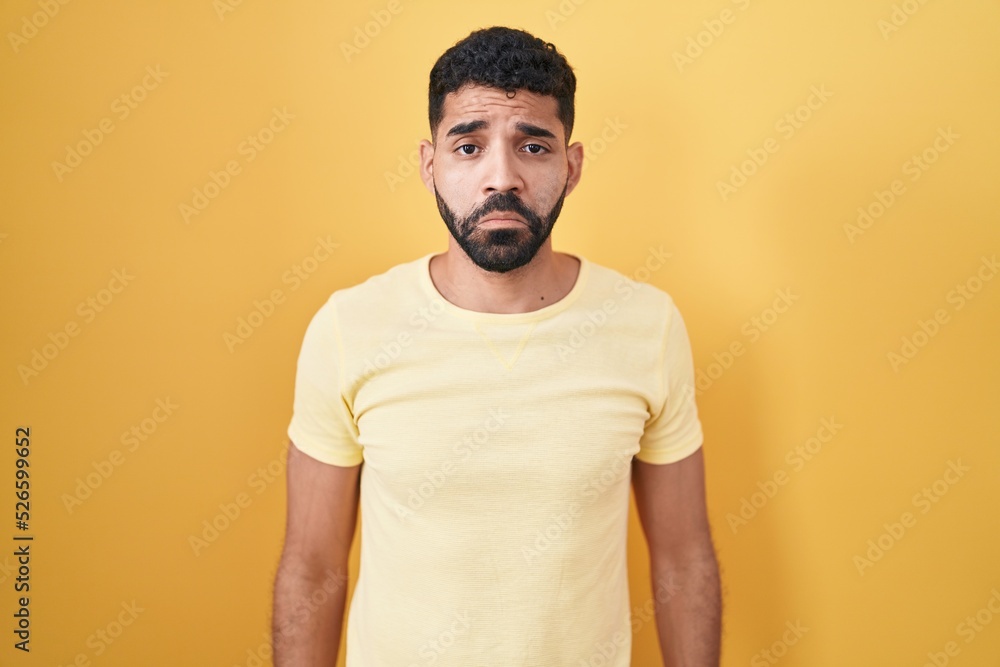 Hispanic man with beard standing over yellow background depressed and worry for distress, crying angry and afraid. sad expression. Hispanic man with beard standing over yellow background depressed and worry for distress, crying angry and afraid. sad expression.