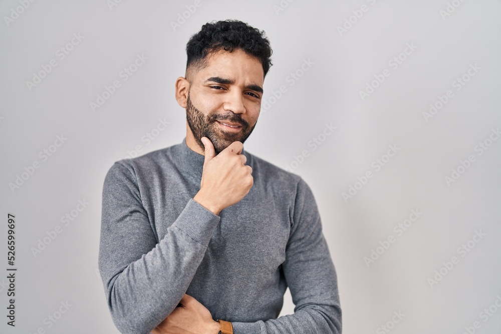 Hispanic man with beard standing over white background looking confident at the camera smiling with crossed arms and hand raised on chin. thinking positive. Hispanic man with beard standing over white background looking confident at the camera smiling with crossed arms and hand raised on chin. thinking positive.