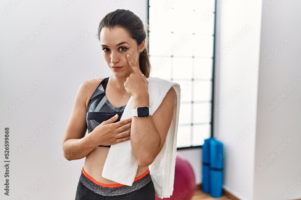 Young brunette woman wearing sportswear and towel at the gym pointing to the eye watching you gesture, suspicious expression Young brunette woman wearing sportswear and towel at the gym pointing to the eye watching you gesture, suspicious expression