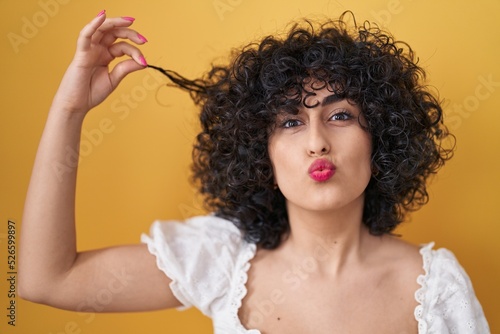 Photographie Young brunette woman with curly hair holding curl looking at the camera blowing a kiss being lovely and sexy