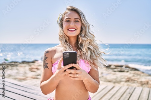 Young blonde girl wearing bikini using smartphone at the beach.