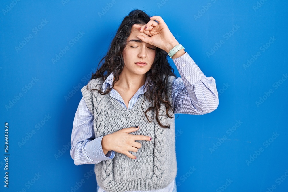 Young brunette woman standing over blue background touching forehead for illness and fever, flu and cold, virus sick Young brunette woman standing over blue background touching forehead for illness and fever, flu and cold, virus sick