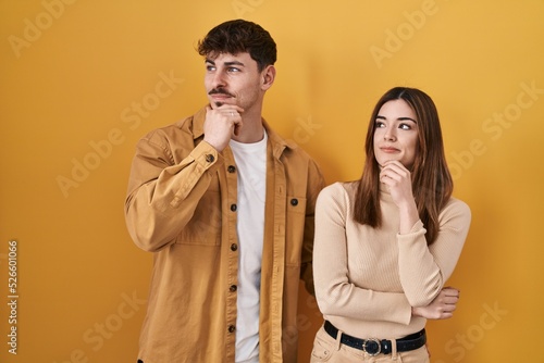Young hispanic couple standing over yellow background looking confident at the camera smiling with crossed arms and hand raised on chin. thinking positive. © Krakenimages.com