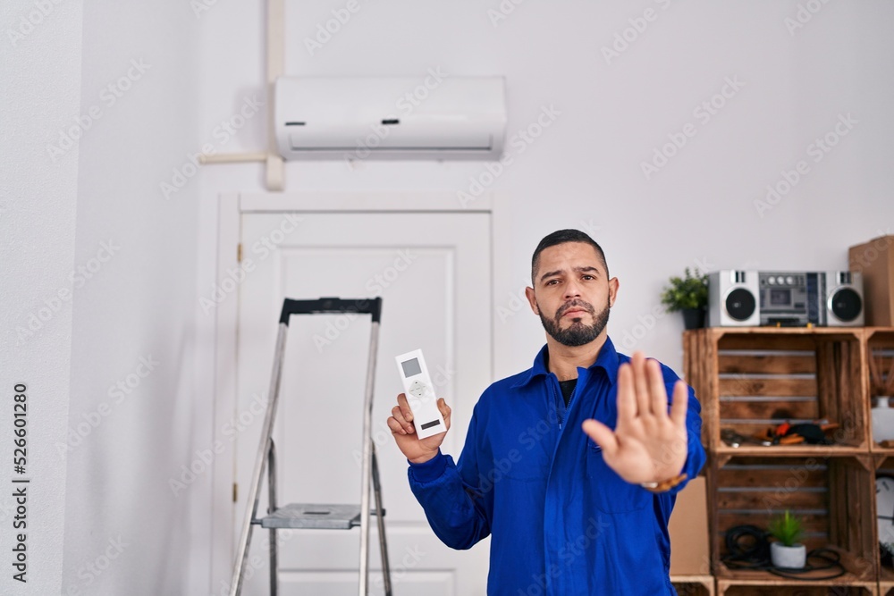 Hispanic repairman working with air conditioner with open hand doing stop sign with serious and confident expression, defense gesture
