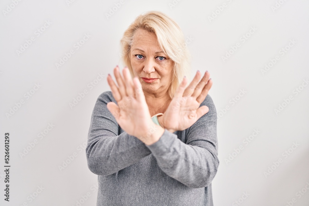 Middle age caucasian woman standing over white background rejection expression crossing arms and palms doing negative sign, angry face Middle age caucasian woman standing over white background rejection expression crossing arms and palms doing negative sign, angry face