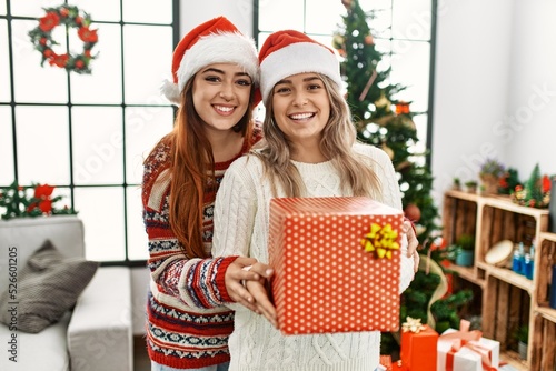 Woman couple hugging each other holding gift standing by christmas tree at home