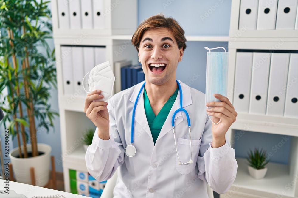 Young doctor man holding two safety mask celebrating crazy and amazed for success with open eyes screaming excited. Young doctor man holding two safety mask celebrating crazy and amazed for success with open eyes screaming excited.