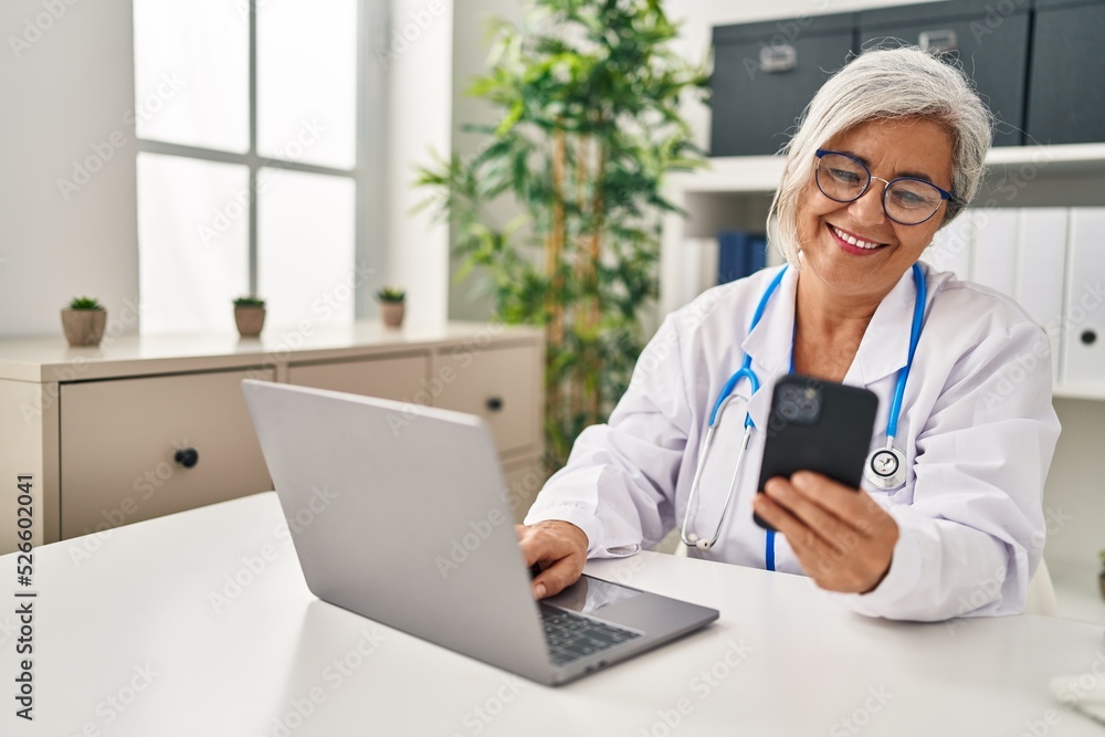 Middle age woman wearing doctor uniform using smartphone at clinic Middle age woman wearing doctor uniform using smartphone at clinic