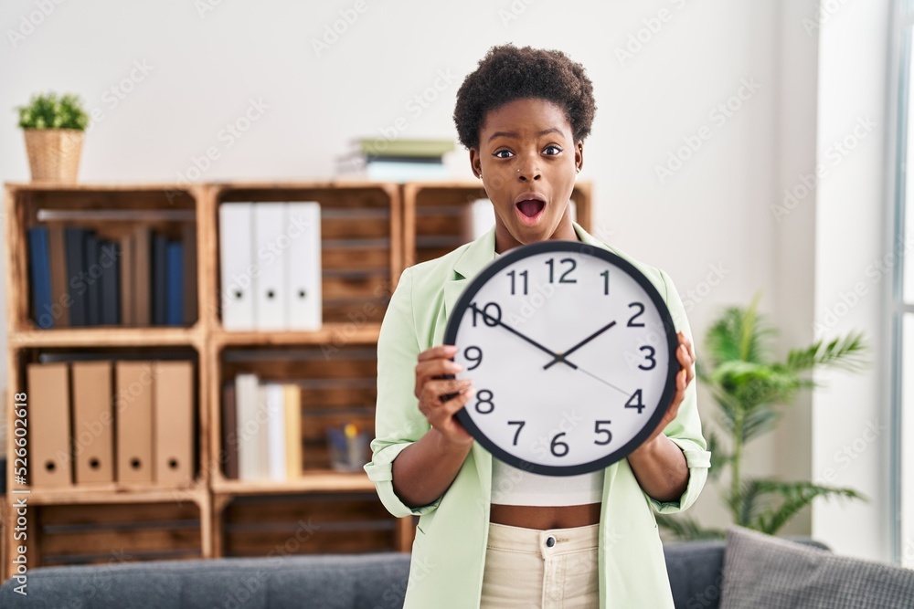 African american woman holding big clock celebrating crazy and amazed for success with open eyes screaming excited. African american woman holding big clock celebrating crazy and amazed for success with open eyes screaming excited.
