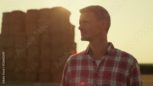 Farm worker golden sunlight at hay bales closeup. Pensive man observing harvest